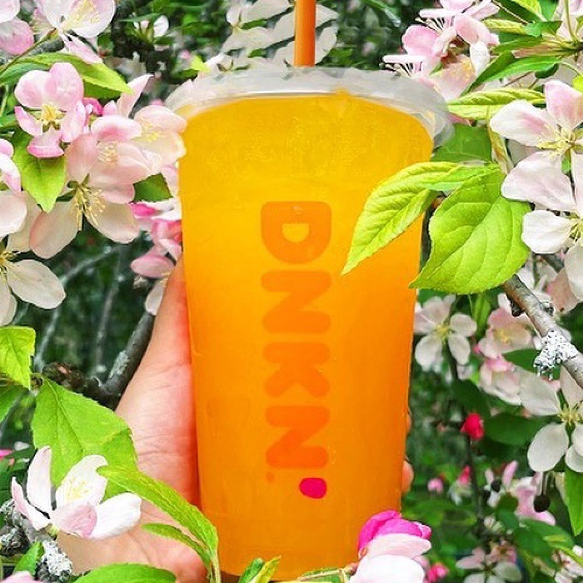 hand holding cup of mango pineapple dunkin refresher surrounded by flowers