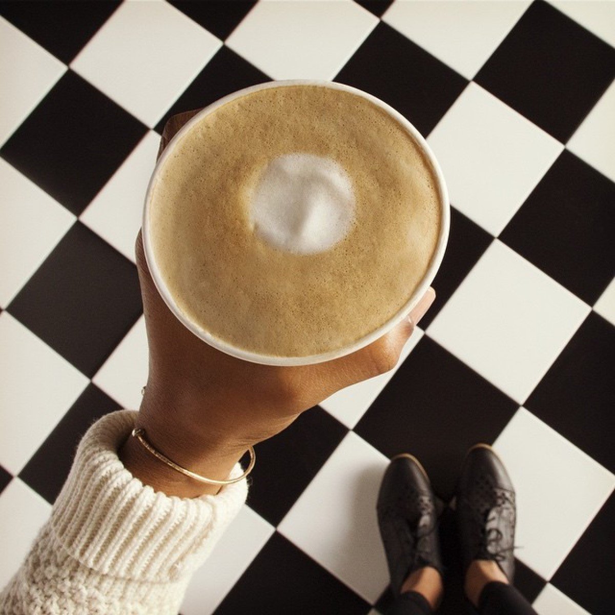 hand holding cup of starbucks flat white checkered tiles in background