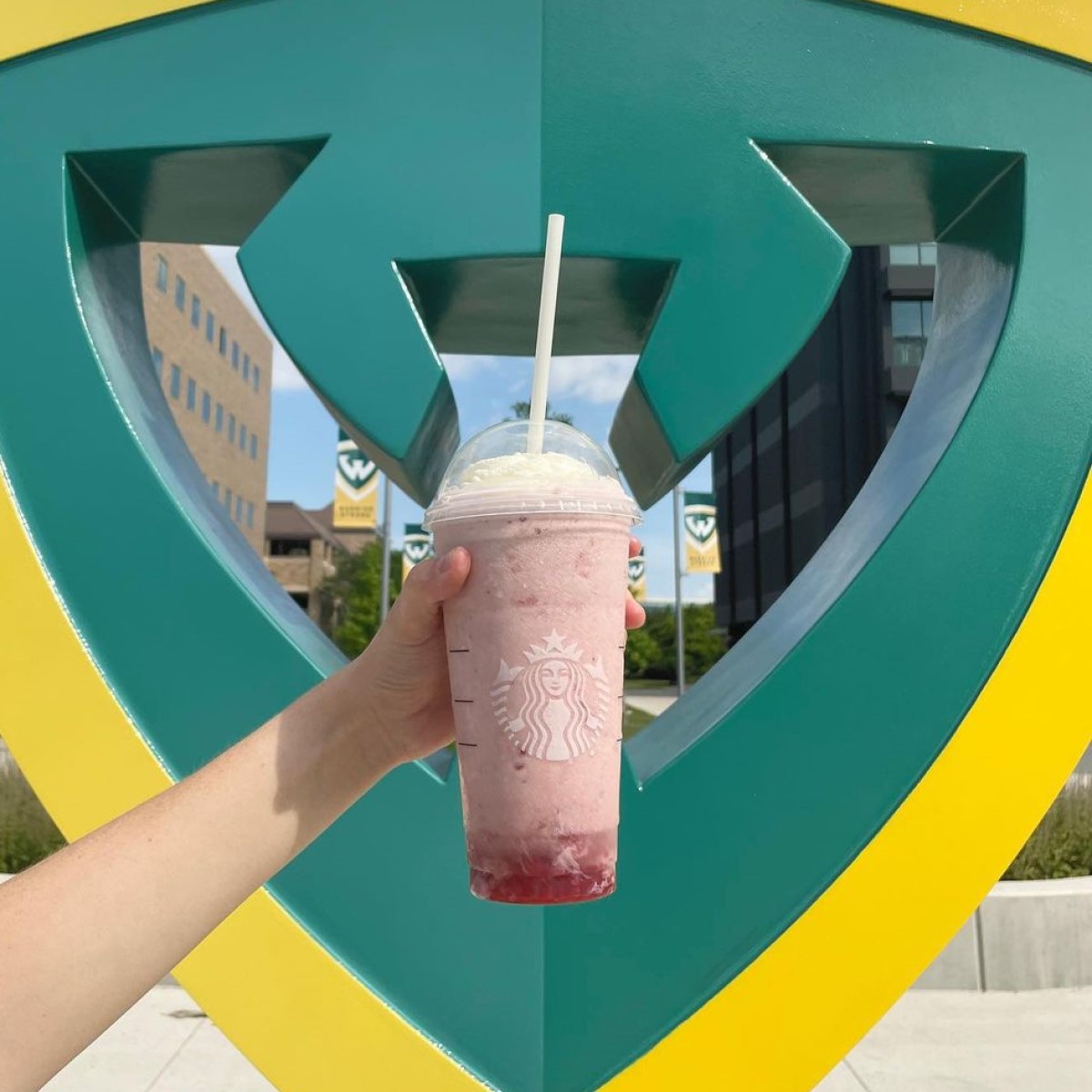 hand holding cup of starbucks strawberry creme frappuccino in front of state college statue