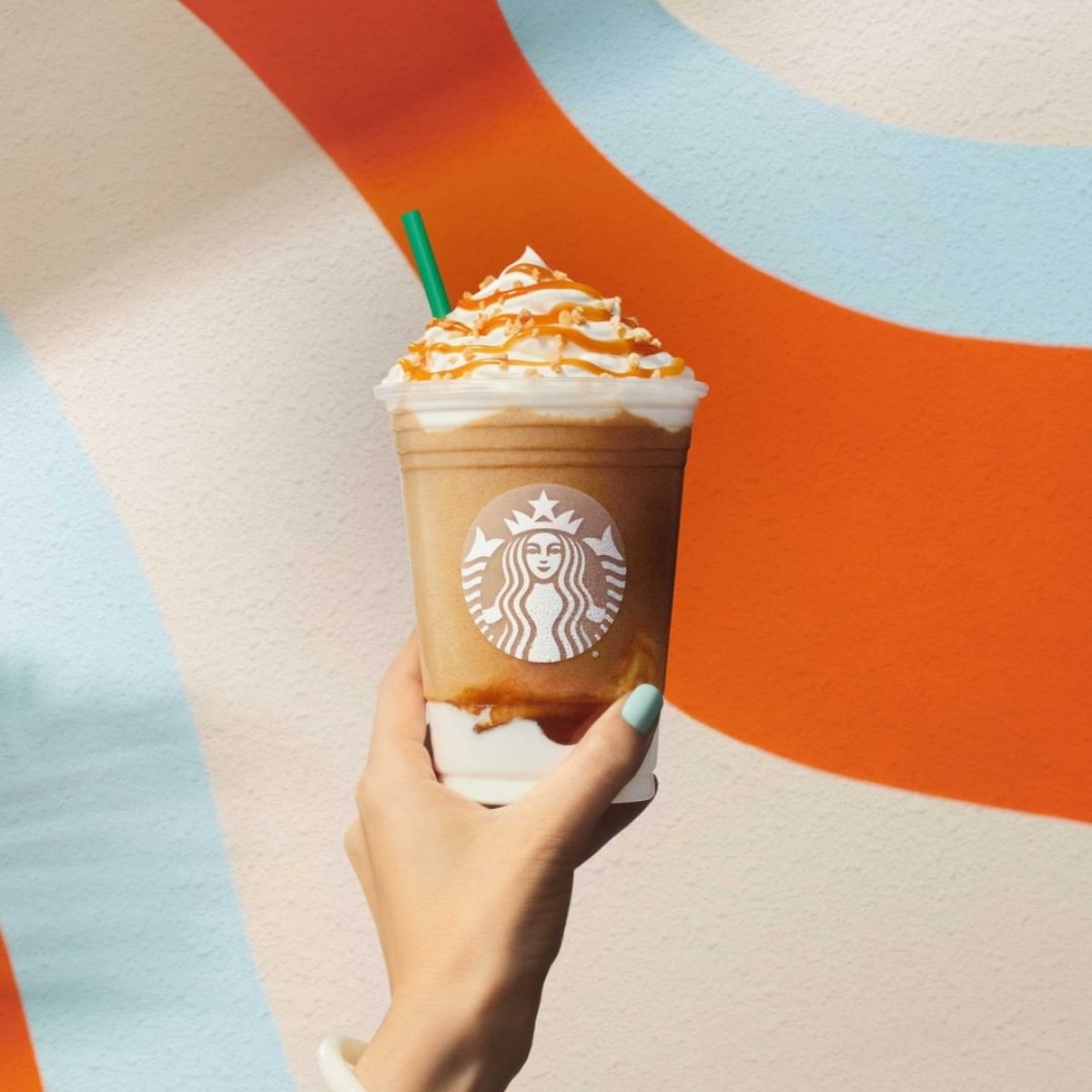 hand holding up Caramel Ribbon Crunch Creme Frappuccino in front of colorful mural