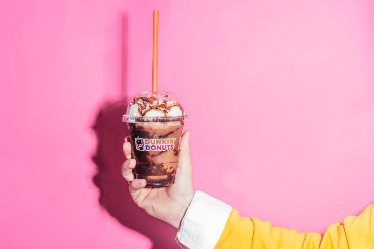 hand holding up cup of duhnkin dunkaccino choco fudge in front of pink background