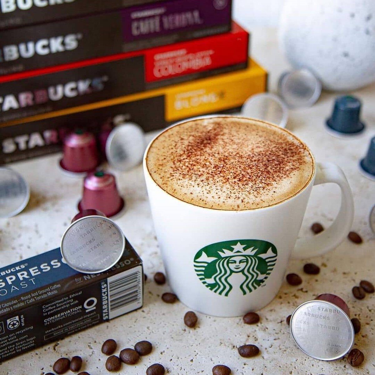 hot cappuccino in white starbucks mug on table with scattered coffee beans