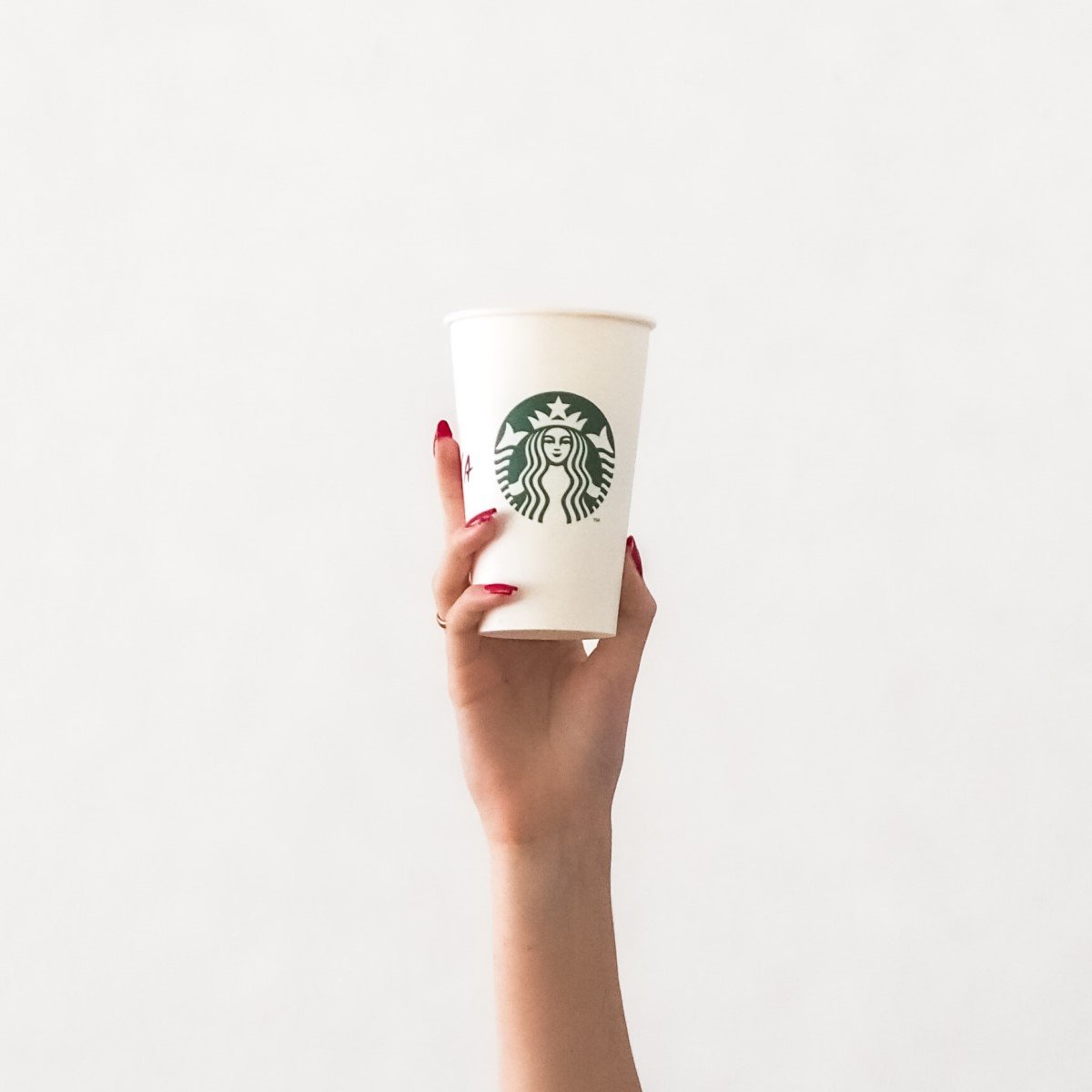 person holding white starbucks paper cup up white background