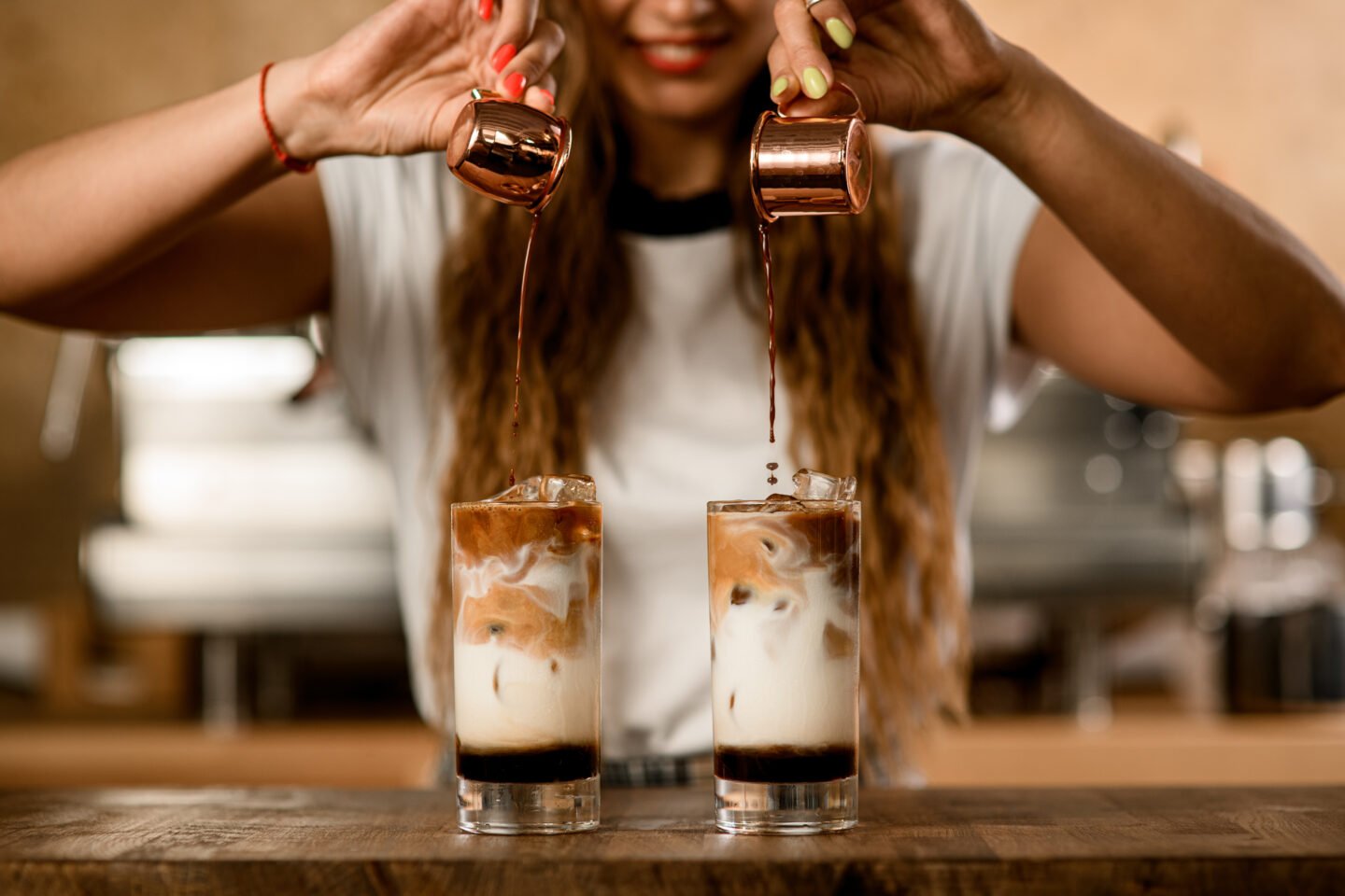 woman-carefully-pours-espresso-from-cups-into-glasses-with-milk-and-syrup
