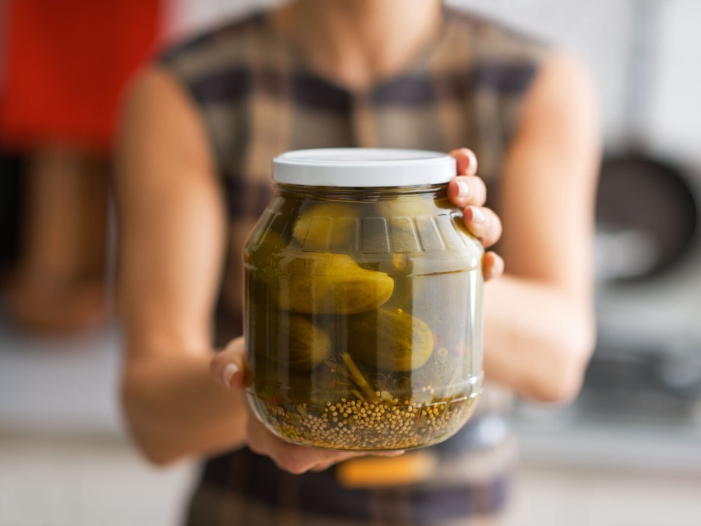 woman presents a jar of pickled cucumbers