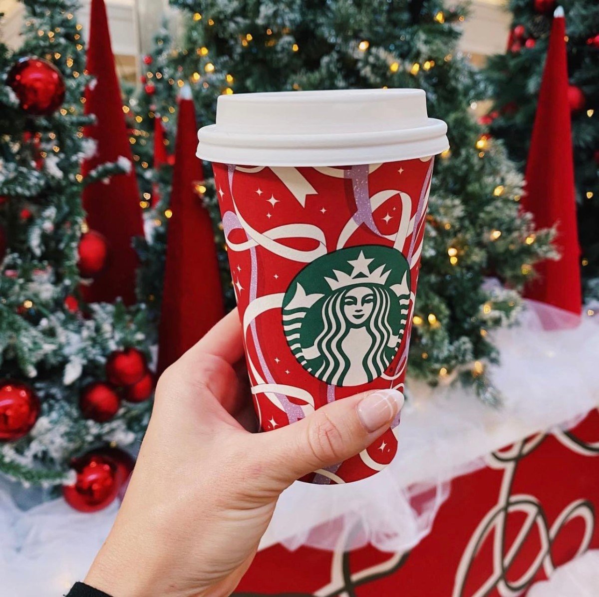 hand holding up cup of white chocolate peppermint mocha in front of christmas tree