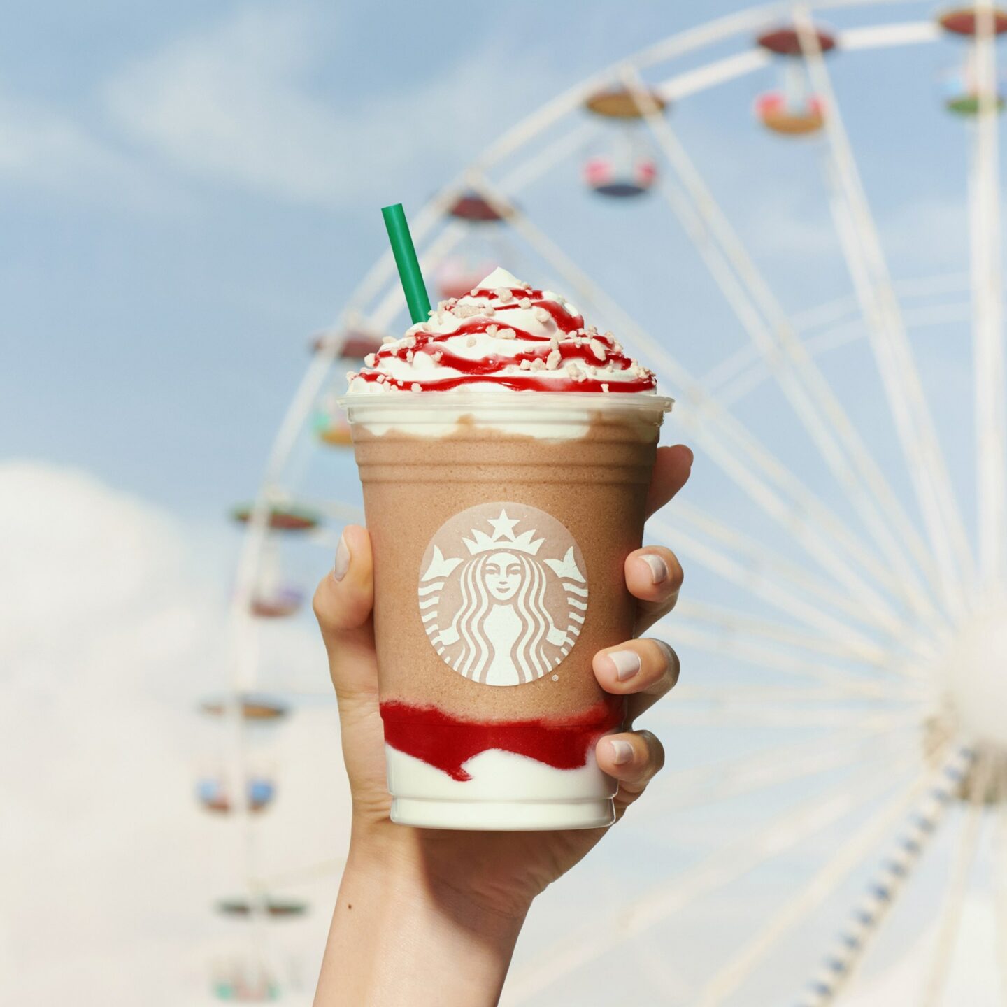 person holding a starbucks drink with a ferris wheel background