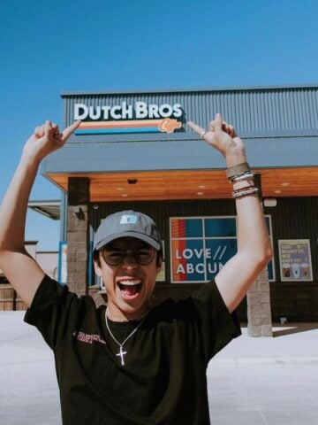 smiling guy pointing to dutch bros sign and logo on store behind him