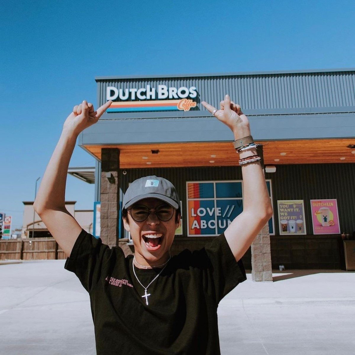 smiling guy pointing to dutch bros sign and logo on store behind him