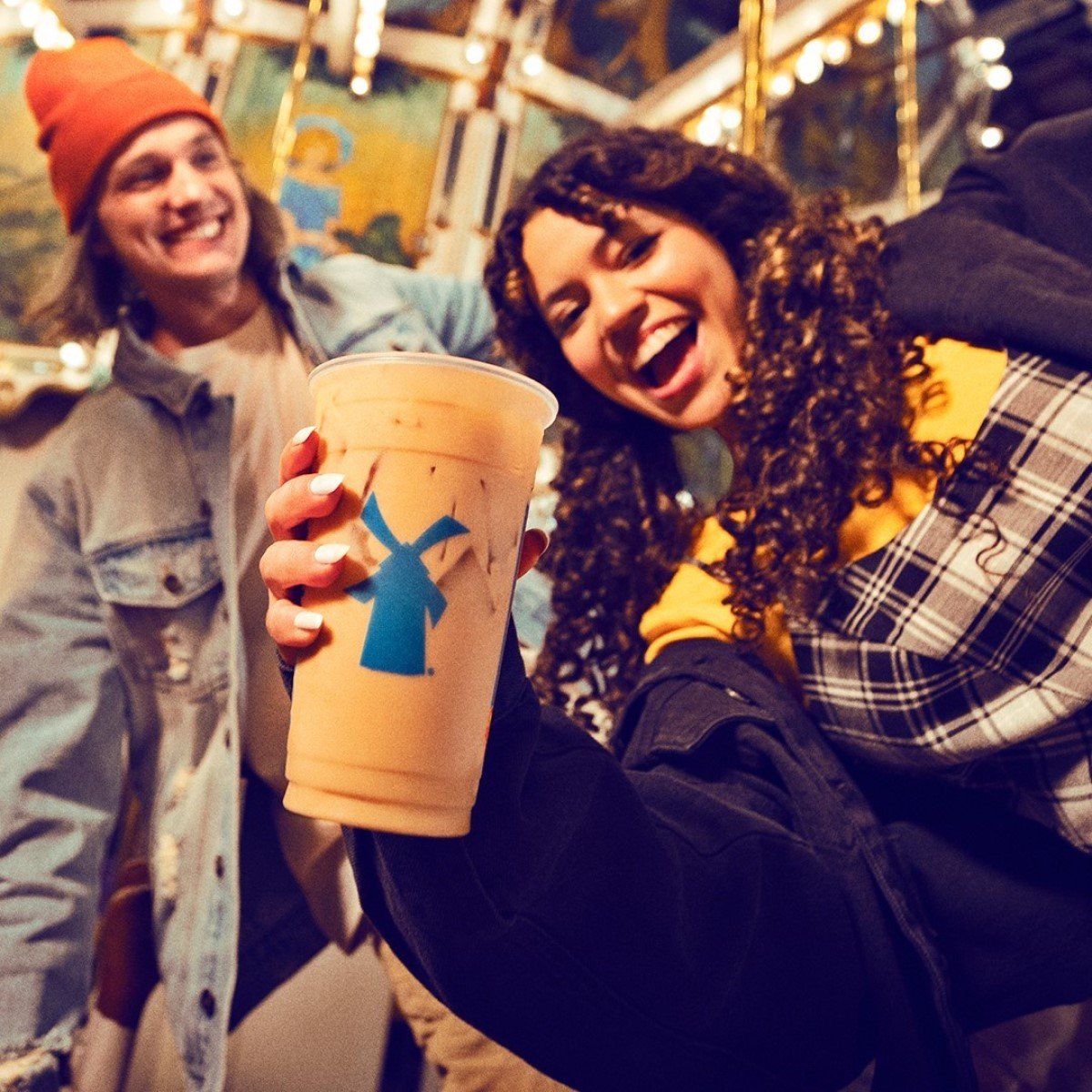 smiling woman holding dutch bros iced cinnamon swirl oat milk latte