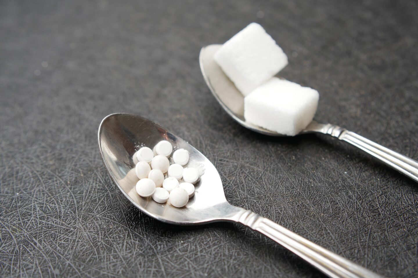 artificial sweetener tablets and sugar cubes in separate spoons