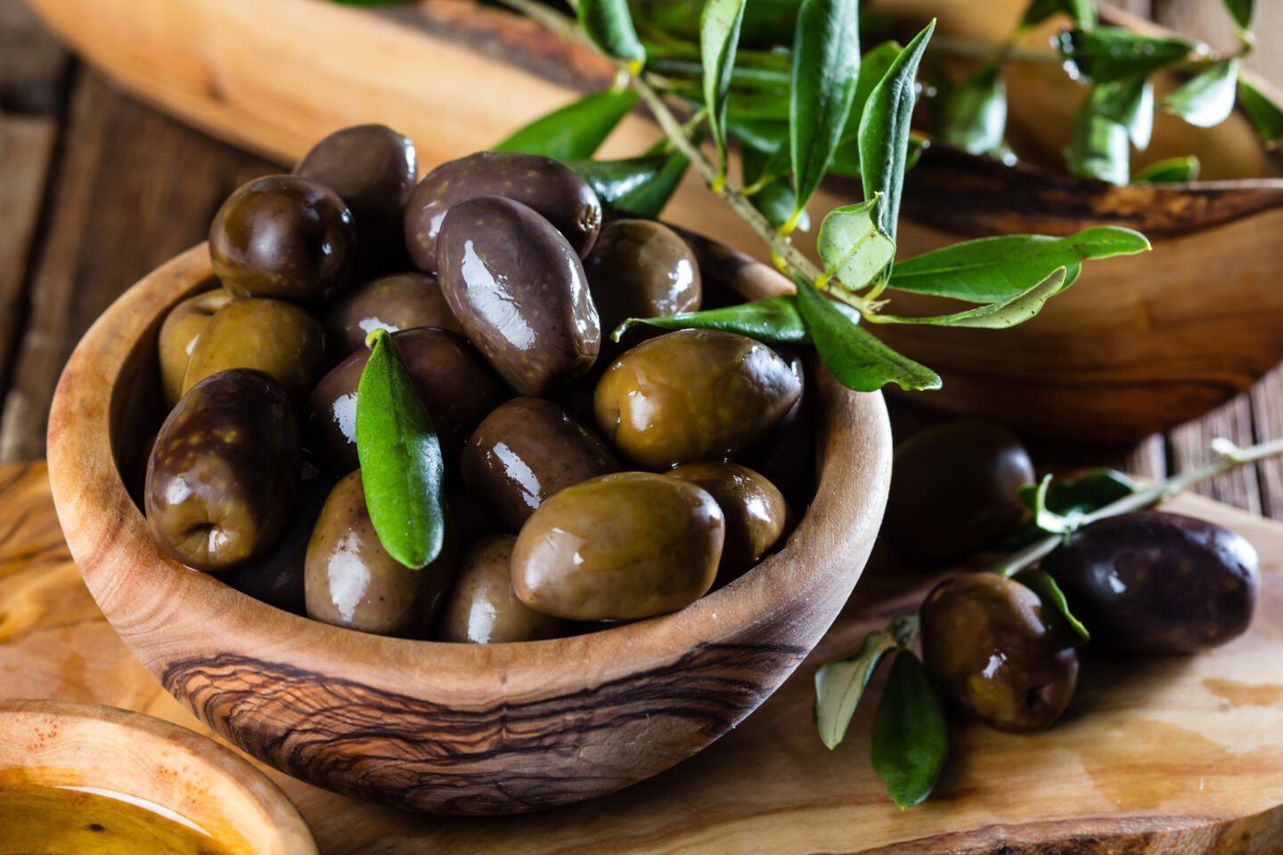 Olives and olive oil in olive wooden bowls, olive tree branch