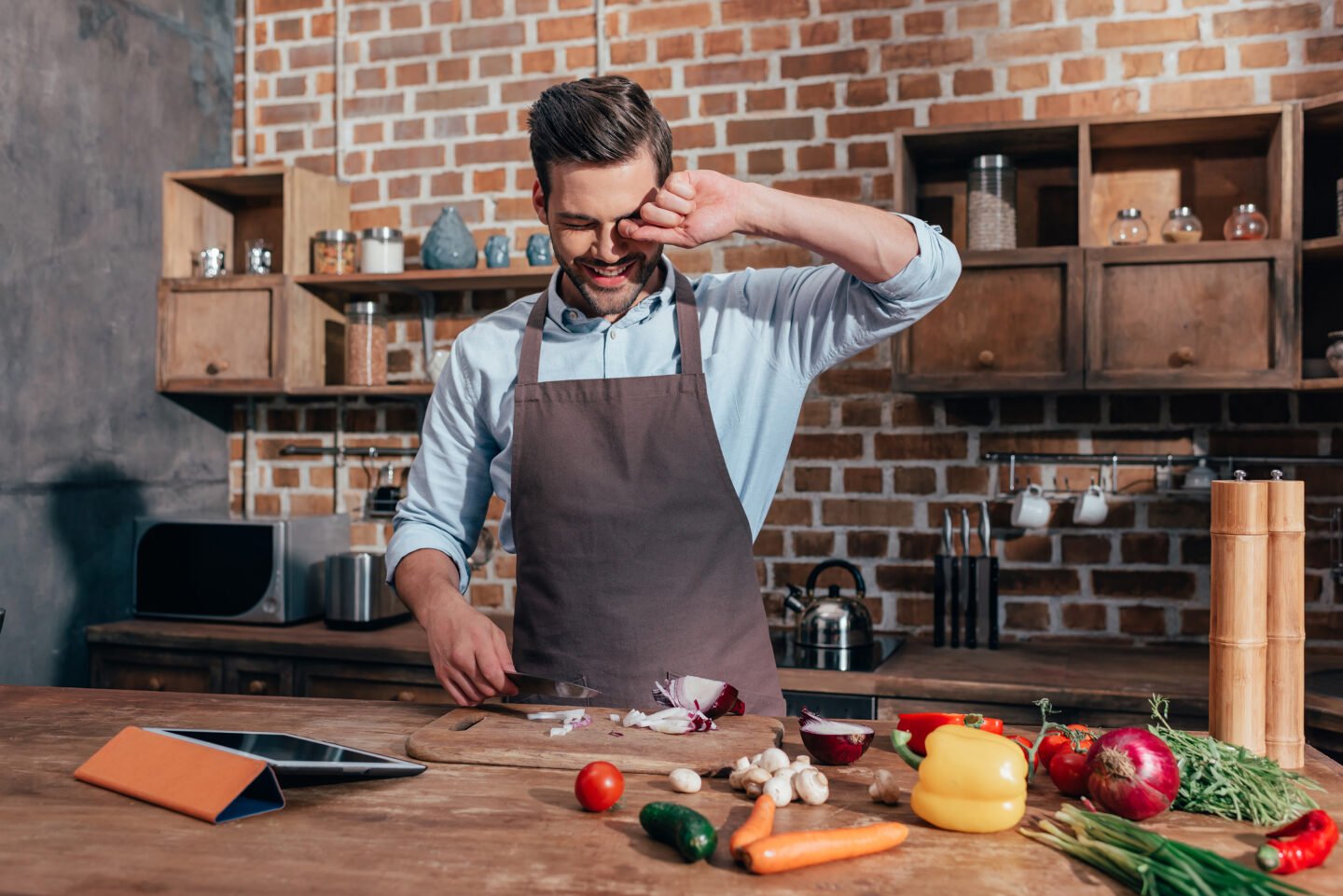 young man crying while cutting onions