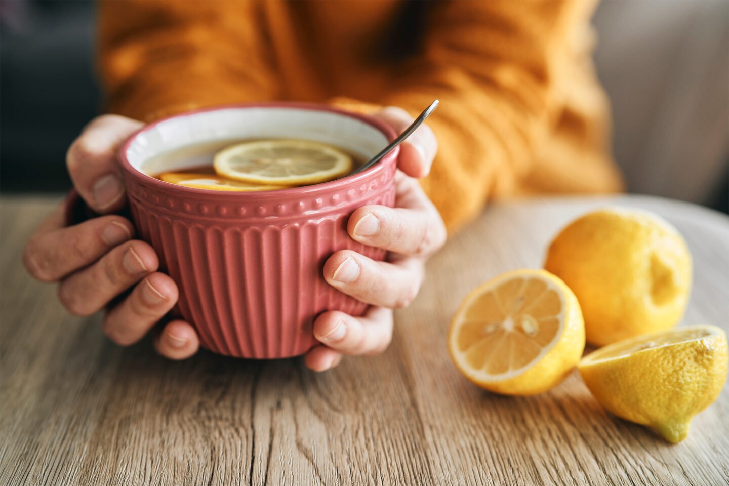 hands holding a big cup of hot tea with lemon slices